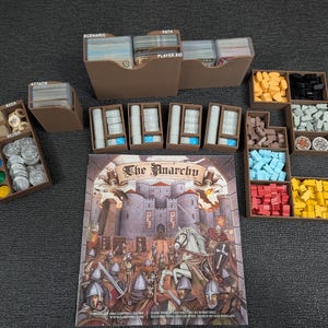 Peut inclure: Un organisateur en bois brun avec des compartiments pour ranger les pièces et les cartes de jeu. L'organisateur est étiqueté avec les mots "Scénario", "Chemin", "Aide du joueur", "Attaque", "Or", "Argent" et "Joueur". L'organisateur est rempli de diverses pièces de jeu, y compris des pièces de monnaie, des jetons et des cartes. Le plateau de jeu est en arrière-plan.