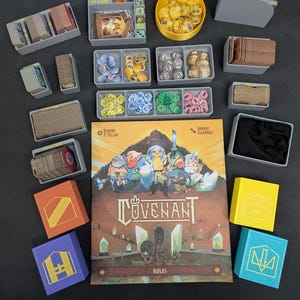 Puede incluir: Juego de mesa "Covenant" con componentes, cartas, fichas, dados y bandejas de almacenamiento. La caja del juego es marrón con una ilustración de fantasía. También hay varias cajas de colores.
