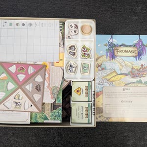 May include: A board game called "Fromage" with a game board, playing pieces, and instruction booklet. The game board is a light brown color with a grid pattern and a light blue border. The playing pieces are made of wood and are painted in various colors. The instruction booklet is a light brown color with a white border and the title "Fromage" printed in black.
