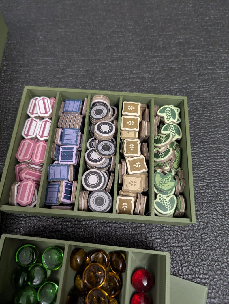 May include: A green organizer box filled with game pieces. The pieces are various shapes and colors, including pink, blue, gray, brown, and green. The box is divided into compartments for easy organization.