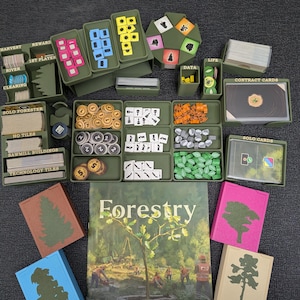 May include: An overhead shot of a board game titled "Forestry" with various components. The game includes rulebooks, cards, tokens, and trays in shades of green, brown, and other colors. The rulebook features a tree graphic and the game's title.