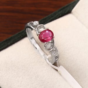 Peut inclure: Bague en argent ornée d'un rubis ovale. La bague présente un design délicat avec de petites pierres d'accent et des détails complexes. La bague est présentée dans un écrin à bijoux.