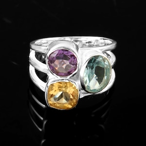 May include: A silver ring featuring three gemstones: a purple amethyst, a light blue aquamarine, and a yellow citrine.