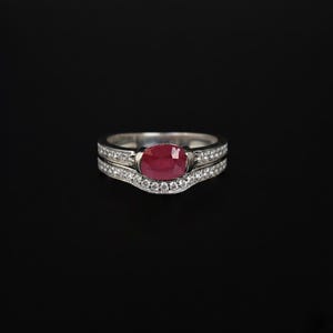 This exquisite bridal set features a vibrant, oval-cut ruby nestled within a shimmering halo of pavé-set diamonds. Crafted in high-quality white gold, the contoured wedding band fits seamlessly against the engagement ring, creating a sophisticated, layered look. Whether you are celebrating a July birthday, a 40th anniversary, or a romantic proposal, this set offers a bold pop of color and classic elegance that stands out from the crowd.