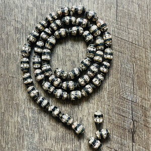 May include: A long strand of black and white patterned beads with gold accents. The beads are oval shaped and are made of a mosaic of small white and black squares.