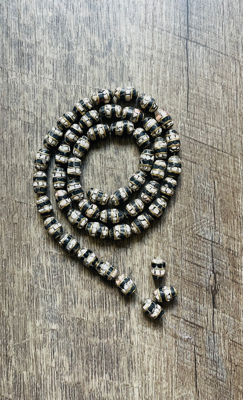 May include: A long strand of black and white patterned beads with gold accents. The beads are oval shaped and are made of a mosaic of small white and black squares.
