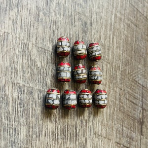May include: Twelve red, white, and gold cylindrical beads with a geometric pattern. The beads are arranged in three rows of four beads each.