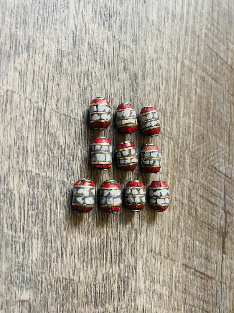 May include: Twelve red, white, and gold cylindrical beads with a geometric pattern. The beads are arranged in three rows of four beads each.