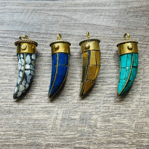 May include: Four decorative pendants shaped like tusks, each with a different colored mosaic design. The pendants are made of brass and feature a gold, blue, turquoise, and white mosaic pattern.