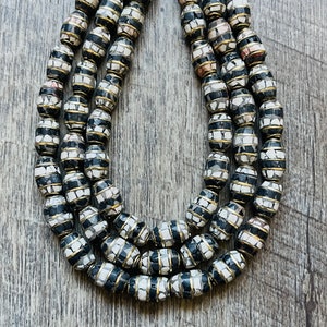 May include: A multi-strand necklace made of oval-shaped beads with a black and white mosaic pattern. The beads are accented with a thin gold band.