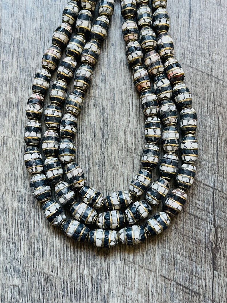 May include: A multi-strand necklace made of oval-shaped beads with a black and white mosaic pattern. The beads are accented with a thin gold band.