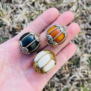 Puede incluir: Tres adornos redondos decorativos con intrincados diseños de metalistería. Los adornos están hechos de diferentes materiales, incluyendo negro, blanco y ámbar.
