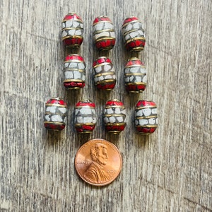 May include: Ten red and white oval-shaped beads with a gold trim. The beads are approximately the size of a US penny.