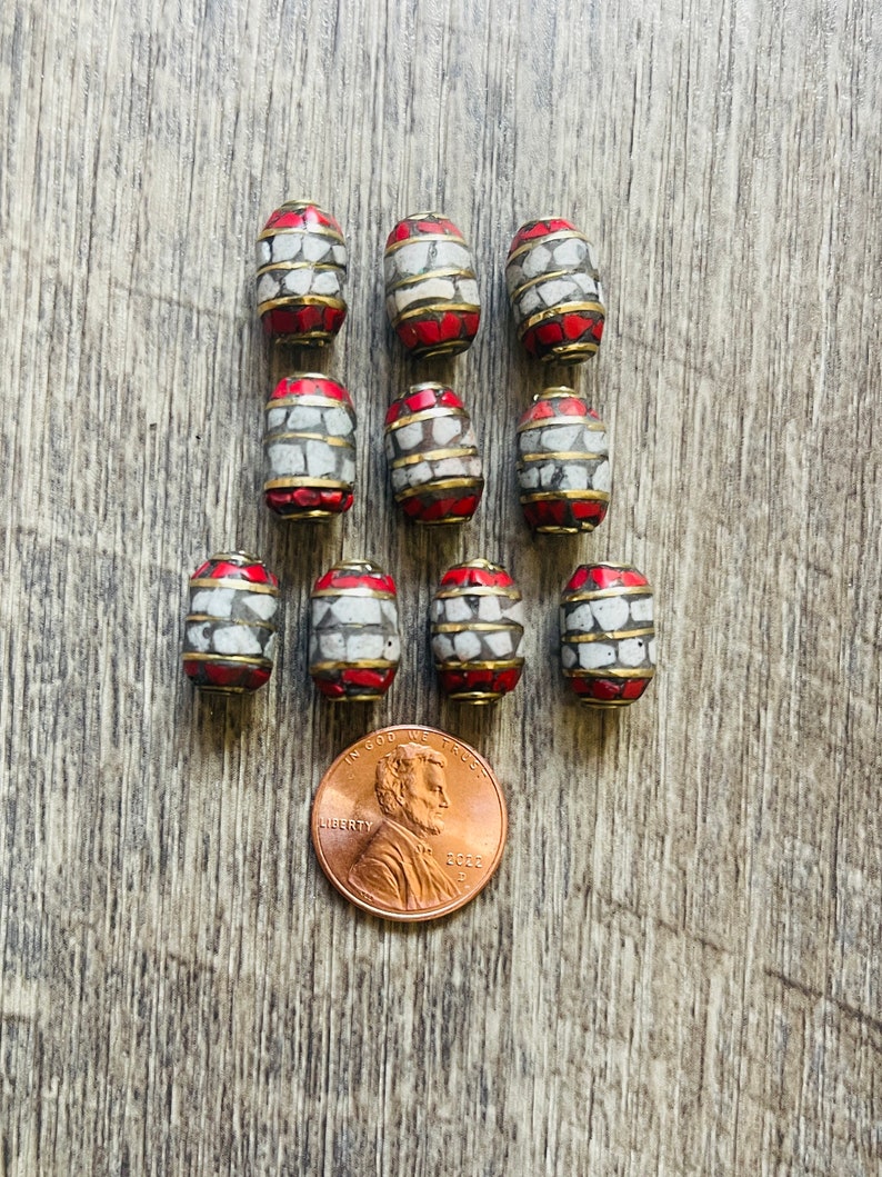 May include: Ten red and white oval-shaped beads with a gold trim. The beads are approximately the size of a US penny.