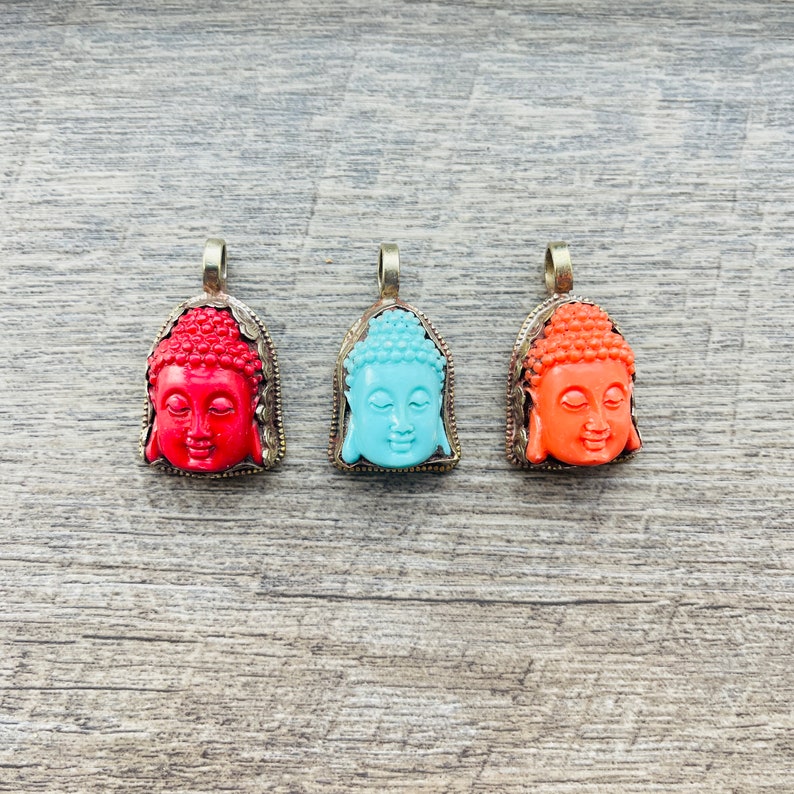 May include: Three silver pendants with Buddha faces. The pendants are in red, blue, and orange.