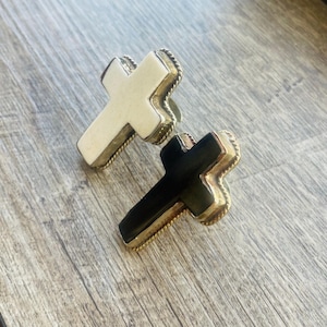 Puede incluir: Dos pendientes de cruz de oro, uno con acabado de esmalte blanco y otro con acabado de esmalte negro.