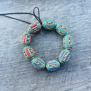 May include: A bracelet made of round beads with intricate designs. The beads are a mix of turquoise, blue, and red colors. The bracelet is strung on a black cord.