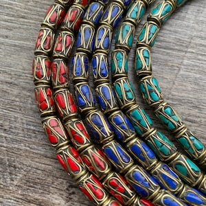 May include: A necklace composed of cylindrical beads featuring brass metal casings with inlaid stone fragments. The beads are arranged in rows of red, blue, and turquoise colors, showcasing a mosaic pattern within the metallic frame structure.