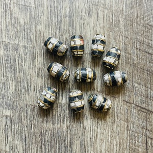 May include: A collection of ten oval-shaped beads with a black and white mosaic pattern. The beads are accented with a thin gold band around the center.