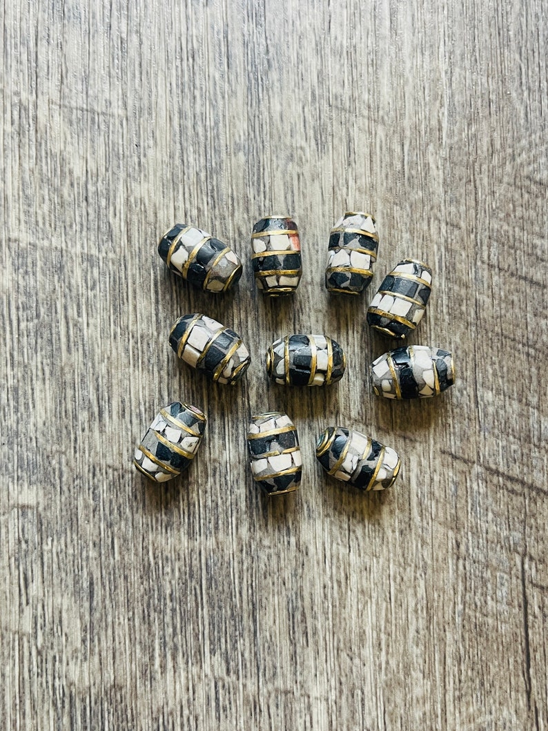 May include: A collection of ten oval-shaped beads with a black and white mosaic pattern. The beads are accented with a thin gold band around the center.
