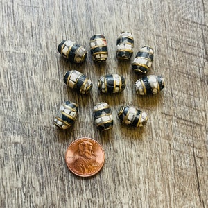May include: A collection of 10 black and white mosaic barrel-shaped beads with gold trim. The beads are approximately the size of a US penny.