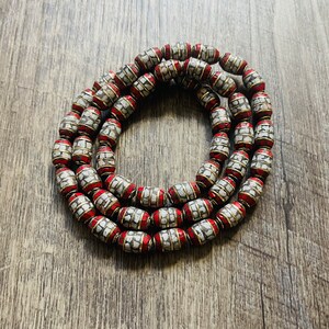 May include: A strand of white and red beads with a gold trim. The beads are oval shaped and have a textured surface.