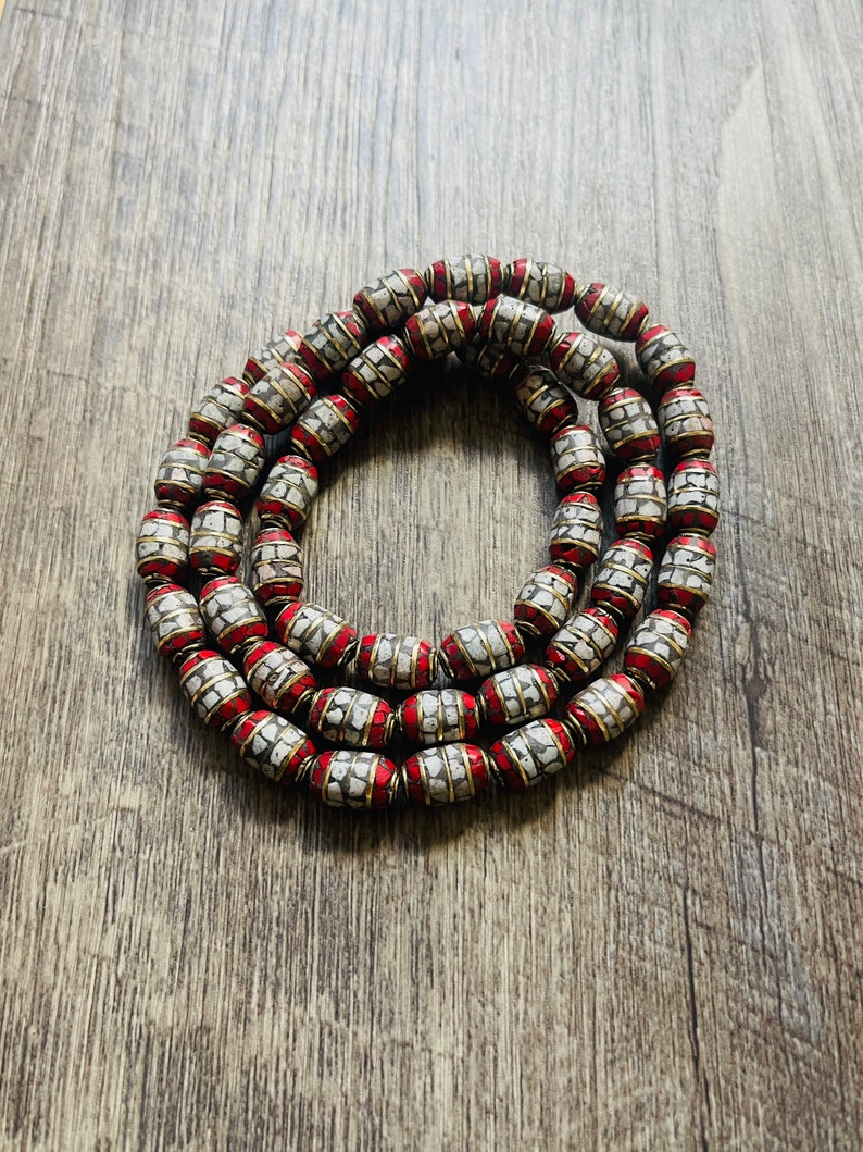 May include: A strand of white and red beads with a gold trim. The beads are oval shaped and have a textured surface.
