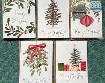 May include: Five Christmas cards with watercolour illustrations. Designs include mistletoe, Christmas trees, and baubles. Each card features the text "Merry Christmas" in a handwritten style. The cards have a white background with a brown border.