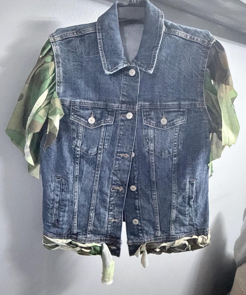 Puede incluir: Un chaleco de mezclilla azul oscuro con cuello cl&aacute;sico, cierre frontal de botones met&aacute;licos y dos bolsillos en el pecho. La prenda est&aacute; decorada con mangas con volantes de tela de camuflaje verde y marr&oacute;n y un dobladillo a juego con lazos.