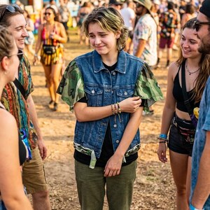 Puede incluir: Un chaleco de mezclilla azul con mangas de volantes y dobladillo en estampado de camuflaje. El chaleco tiene cuello cl&aacute;sico, botones met&aacute;licos plateados en la parte delantera y dos bolsillos en el pecho. Se lleva sobre una camiseta negra y pantalones verde oliva.