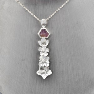 May include: A silver necklace with a pendant featuring a pink gemstone surrounded by silver flowers.