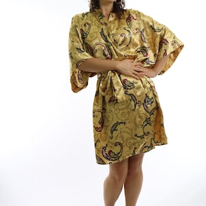May include: A golden-yellow kimono-style robe with a paisley pattern in shades of blue, red, and green. The robe is tied at the waist and worn with black ankle-strap heels. The background is white.