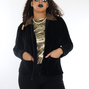 Puede incluir: Chaqueta negra de terciopelo con cremallera y cuello con estampado de leopardo. La chaqueta tiene dos bolsillos delanteros y se combina con pantalones negros. La persona de la imagen lleva gafas de sol y una camiseta dorada.