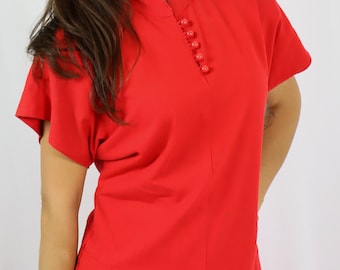 May include: A bright red two-piece outfit. The top has a mandarin collar and short sleeves, with a row of buttons down the front. The skirt features a pleated design on the side and is also buttoned. The outfit is made of a smooth, solid fabric.