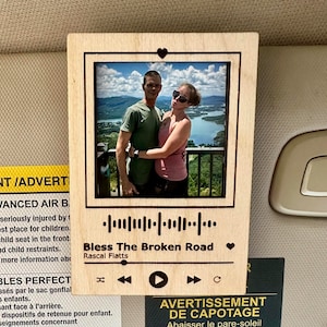 May include: A wooden photo frame with a picture of a couple embracing, set against a scenic backdrop. The frame features a music waveform design with the song title "Bless The Broken Road" by Rascal Flatts.