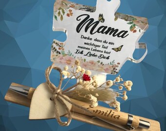 May include: A clear acrylic puzzle piece with a floral design and the text "Mama Danke dass du ein wichtiger Teil meines Lebens bist Ich Liebe Dich". A wooden pen with the name "Emilia" engraved on it is included.