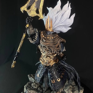 May include: A detailed figurine of a character from the video game Dark Souls. The figure is wearing a golden armor with a black cape and a white crown. The figure is holding a large golden spear with a black handle. The figure is standing on a rocky base.