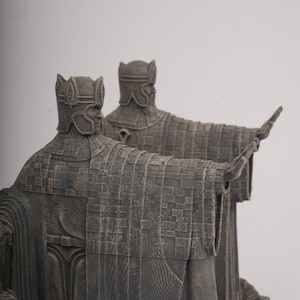 May include: Two statues of figures in ornate armour and helmets, with arms outstretched. The statues are a dark grey colour and appear to be made of stone or a similar material. The figures are standing on a stone base.
