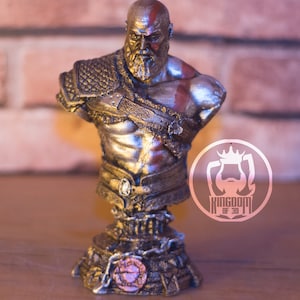May include: A detailed bust of a muscular, bearded figure with a red painted stripe on his head and face. The figure wears ornate armor and has a stern expression. The bust is on a decorative base with the text "KINGDOM OF 3D".