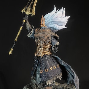 May include: A detailed figurine of a warrior in a gold and black armor, holding a large golden spear. The warrior has long white hair and a crown. The figurine is standing on a rocky base.