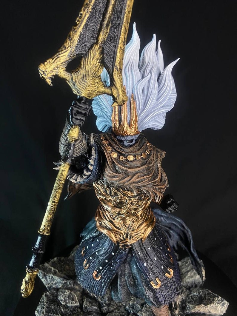 May include: A detailed figurine of a warrior wearing a golden helmet and armor, holding a large, golden weapon with a black handle. The warrior has a white, flowing mane of hair and a dark, flowing cape.