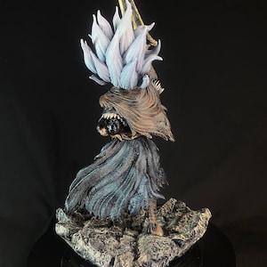 May include: A detailed, hand-painted figurine of a character from a video game. The figure is wearing a flowing, dark blue robe with a gold and white headpiece. The figure is standing on a rocky base.