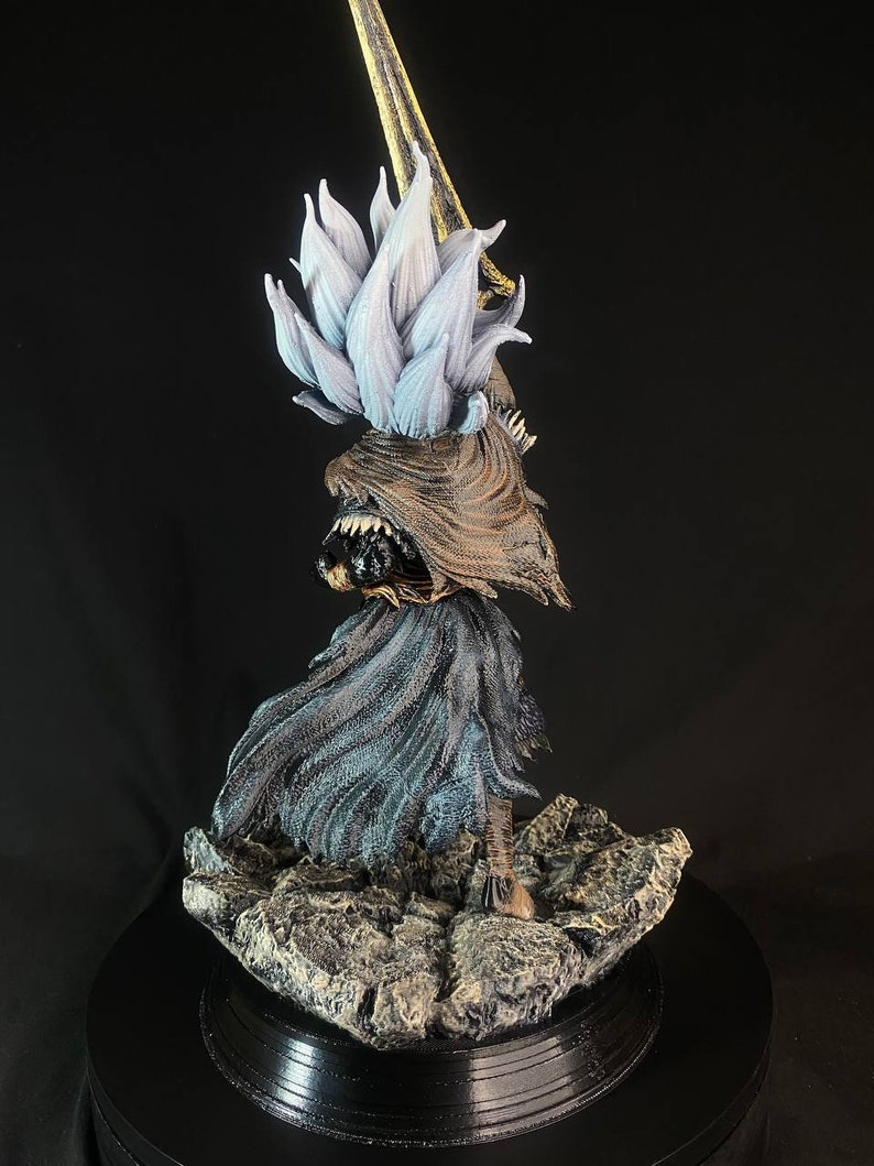 May include: A detailed, hand-painted figurine of a character from a video game. The figure is wearing a flowing, dark blue robe with a gold and white headpiece. The figure is standing on a rocky base.