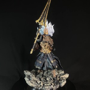 May include: A detailed figurine of The Nameless King from Dark Souls III. The figure is posed holding a spear, with a golden helmet and armor. The figure is standing on a rocky base.