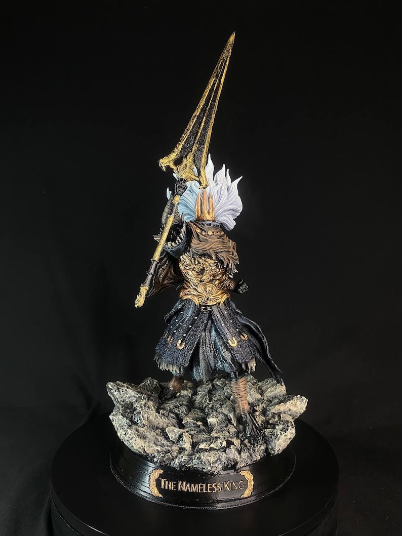 May include: A detailed figurine of The Nameless King from Dark Souls III. The figure is posed holding a spear, with a golden helmet and armor. The figure is standing on a rocky base.