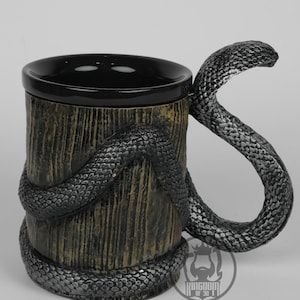 Puede incluir: Taza de cerámica con exterior texturizado con aspecto de madera e interior negro. Una serpiente plateada detallada se enrolla alrededor de la taza y forma el asa. La taza tiene un diseño único inspirado en la fantasía.