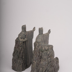 May include: A pair of gray stone-effect bookends featuring figures in medieval armor. Each figure stands atop a rugged, rocky base, wearing a textured tunic and helmet, with one hand extended forward and a sword held at the side of the body.