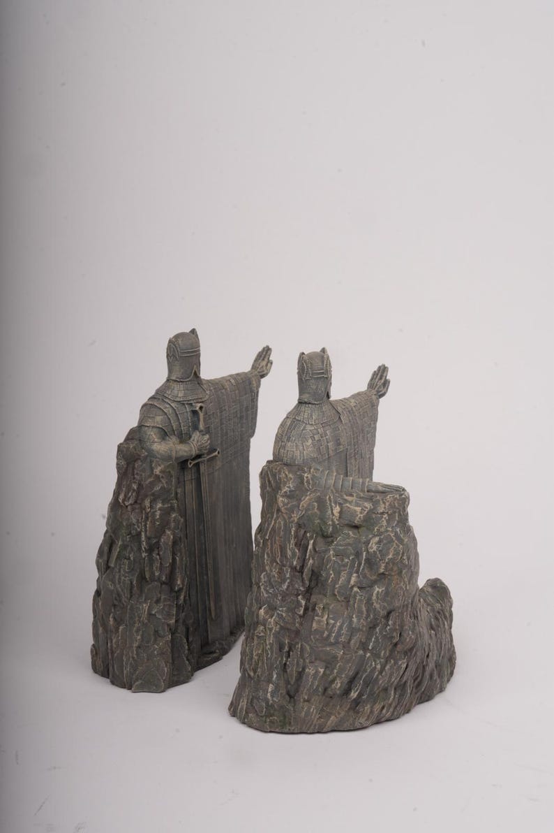 May include: A pair of gray stone-effect bookends featuring figures in medieval armor. Each figure stands atop a rugged, rocky base, wearing a textured tunic and helmet, with one hand extended forward and a sword held at the side of the body.