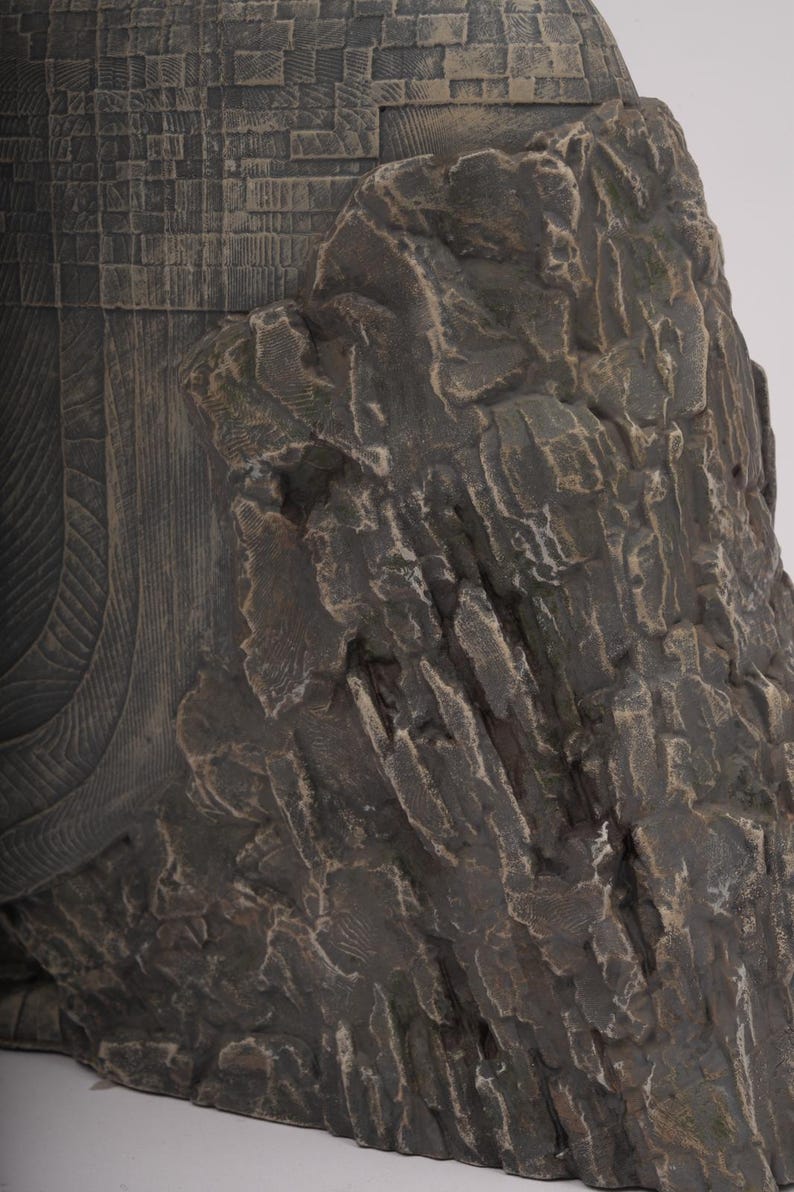 May include: A dark brown sculpture featuring a textured, rugged rock-like formation on the right side, contrasted with a smooth, curved section on the left that displays a detailed, grid-like pattern of small, rectangular, etched indentations.