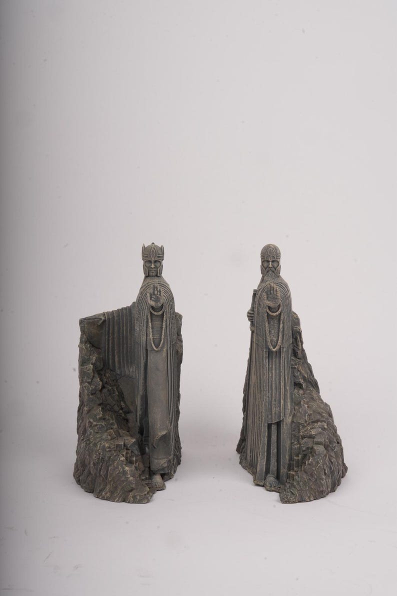 May include: A pair of gray stone-colored bookends featuring sculpted figures of robed individuals standing against jagged rock formations. Each figure is depicted with one arm extended forward, palm open, wearing detailed headgear and long garments.